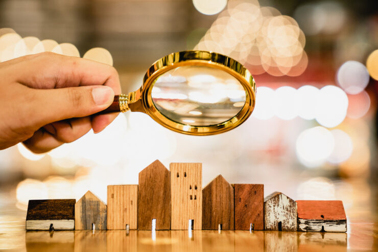 Hand holding magnifying glass and looking at house model, house selection, real estate concept.